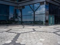 hexagon shaped mosaic pattern in front of glass - covered building, with trees reflecting in window