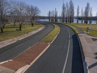 the street curves very wide along the grassy banks of the river side lined with trees and bushes