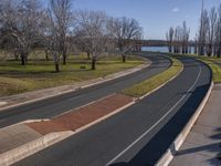 the street curves very wide along the grassy banks of the river side lined with trees and bushes