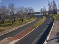 the street curves very wide along the grassy banks of the river side lined with trees and bushes