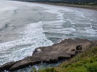 a few people are surfing and in the water near rocks, near the shore line