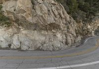 a road winds along a rock face with yellow lines in front of it and a black car driving down the middle