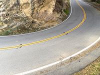 two yellow stripes are on the side of a steep mountain road and two people ride in the middle