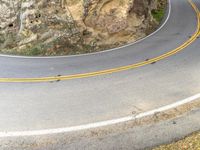 two yellow stripes are on the side of a steep mountain road and two people ride in the middle