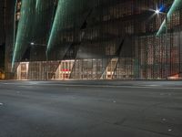 a road with a building that has glass walls at one side and lights on the other side