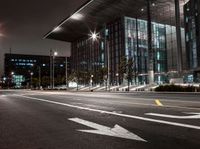 an empty city street with bright lighting at night with traffic signs on it and the building is glass