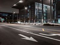 an empty city street with bright lighting at night with traffic signs on it and the building is glass