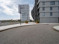 two buildings in an open city with a paved driveway and sidewalk and small planters with trees to the side