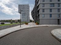 two buildings in an open city with a paved driveway and sidewalk and small planters with trees to the side