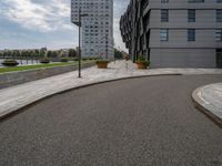 two buildings in an open city with a paved driveway and sidewalk and small planters with trees to the side
