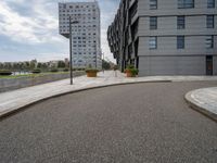 two buildings in an open city with a paved driveway and sidewalk and small planters with trees to the side