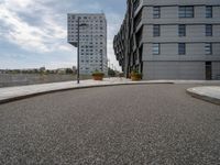 two buildings in an open city with a paved driveway and sidewalk and small planters with trees to the side