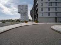 two buildings in an open city with a paved driveway and sidewalk and small planters with trees to the side