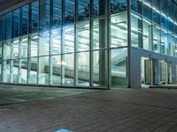 a modern office building with large windows in the front of it at night, next to a bench