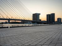 the skyline in the city is filled with tall buildings and bridges by the water and a man standing near a bench on the sidewalk