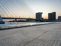 the skyline in the city is filled with tall buildings and bridges by the water and a man standing near a bench on the sidewalk