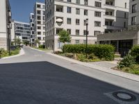 an empty street lined with tall buildings on both sides of the road and shrubs to side