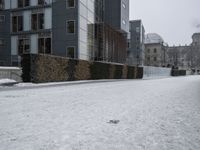 a person that is walking down the street in the snow on the street near some buildings