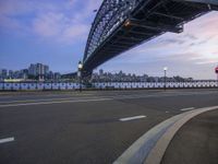 an empty street with cars on it and a big bridge in the background with a city in the distance