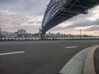 an empty street with cars on it and a big bridge in the background with a city in the distance