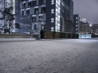 a person standing in a snow covered sidewalk next to a building at night on a cloudy day