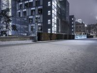 a person standing in a snow covered sidewalk next to a building at night on a cloudy day