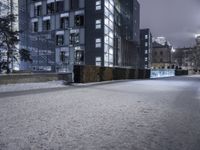 a person standing in a snow covered sidewalk next to a building at night on a cloudy day