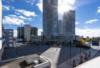 an apartment complex in the sun with parking spaces underneath a clear sky line of tall buildings