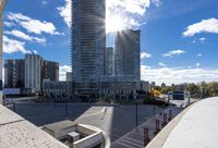 an apartment complex in the sun with parking spaces underneath a clear sky line of tall buildings