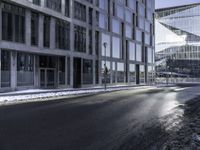 an empty street and snow in front of some high rise buildings near a building with windows