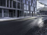 an empty street and snow in front of some high rise buildings near a building with windows