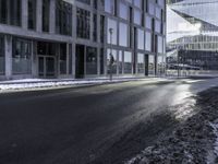 an empty street and snow in front of some high rise buildings near a building with windows