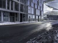 an empty street and snow in front of some high rise buildings near a building with windows