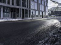 an empty street and snow in front of some high rise buildings near a building with windows