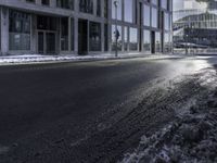 an empty street and snow in front of some high rise buildings near a building with windows