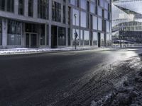 an empty street and snow in front of some high rise buildings near a building with windows