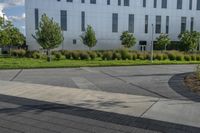 a city street surrounded by grass and tall buildings at the end of a street there is a paved pathway in front of the building