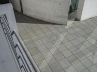 an architectural view of some stone and glass door in the building, with a woman walking by the door, holding a small red umbrella and red purse