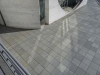 an architectural view of some stone and glass door in the building, with a woman walking by the door, holding a small red umbrella and red purse