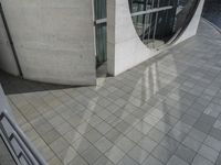 an architectural view of some stone and glass door in the building, with a woman walking by the door, holding a small red umbrella and red purse