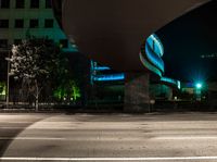 a building is shown behind the road at night while a car drives by on a street