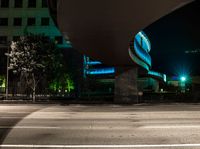 a building is shown behind the road at night while a car drives by on a street