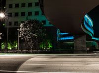 a building is shown behind the road at night while a car drives by on a street