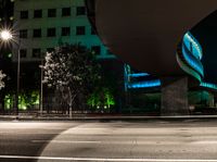 a building is shown behind the road at night while a car drives by on a street