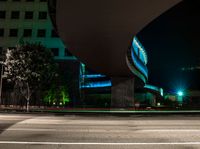 a building is shown behind the road at night while a car drives by on a street