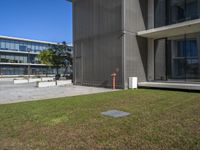 a grassy lawn in front of a building next to a large glass building and sidewalk