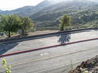 a man rides his motorcycle on a road by some mountains with trees on both sides and a car driving down the street