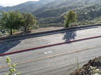 a man rides his motorcycle on a road by some mountains with trees on both sides and a car driving down the street