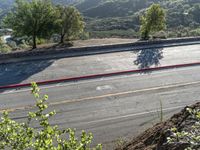 a man rides his motorcycle on a road by some mountains with trees on both sides and a car driving down the street