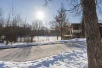 a winter scene with sun shining over the trees and road leading to a parking area